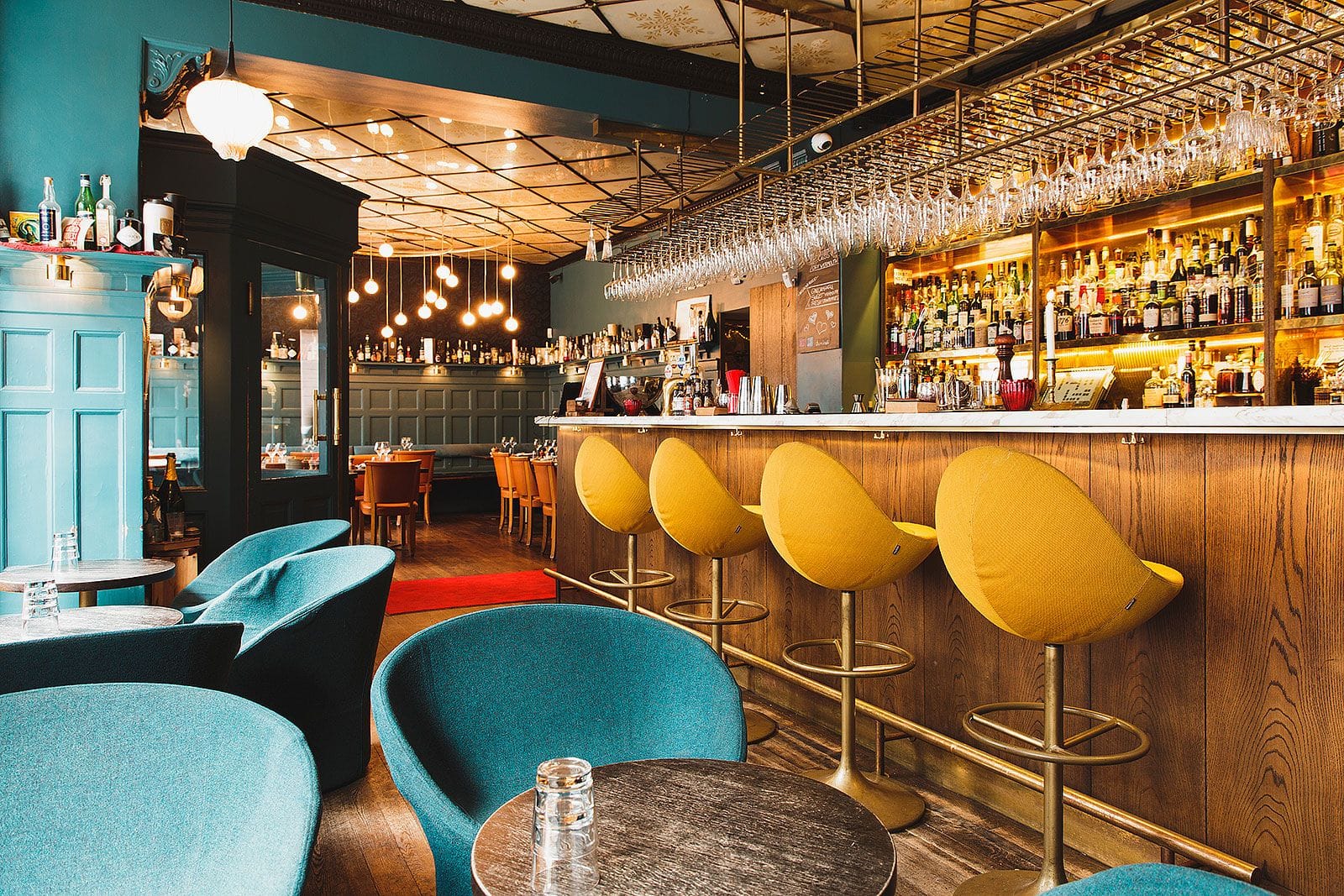 Cocktailbaren på Duvel Café med senapsgula barstolar och flaskvägg